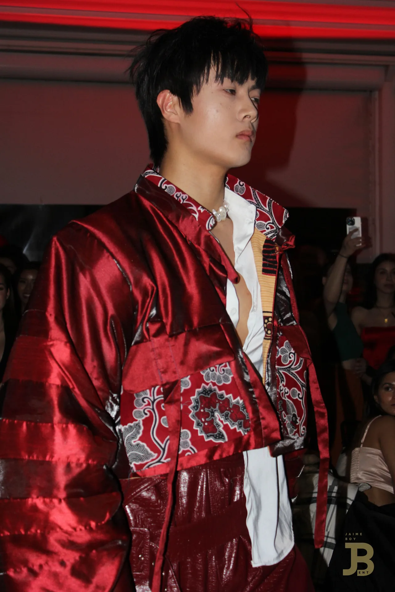 A model in a red satin jacket with paisley panels, photographed close under red light.