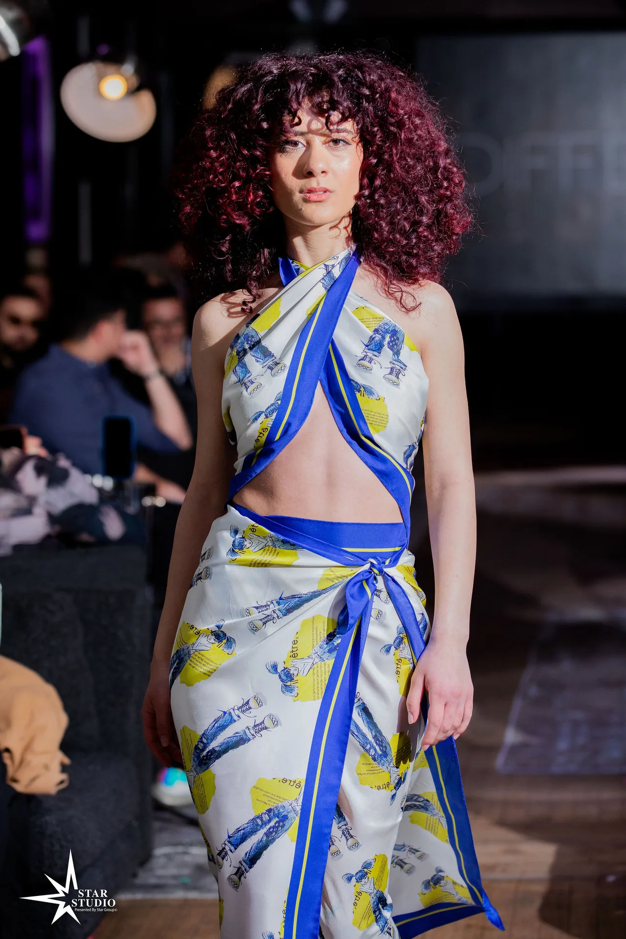 A model in a halter wrap of blue and yellow printed silk with a cut-out waist.
