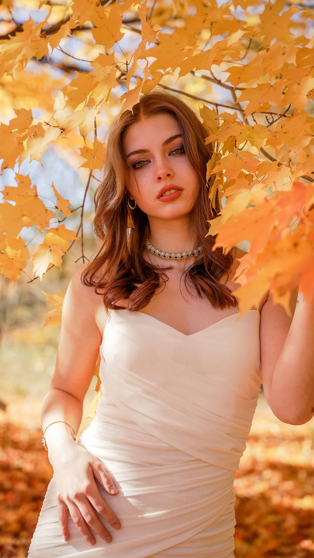 Portrait of a model in an ivory dress framed by orange maple leaves.