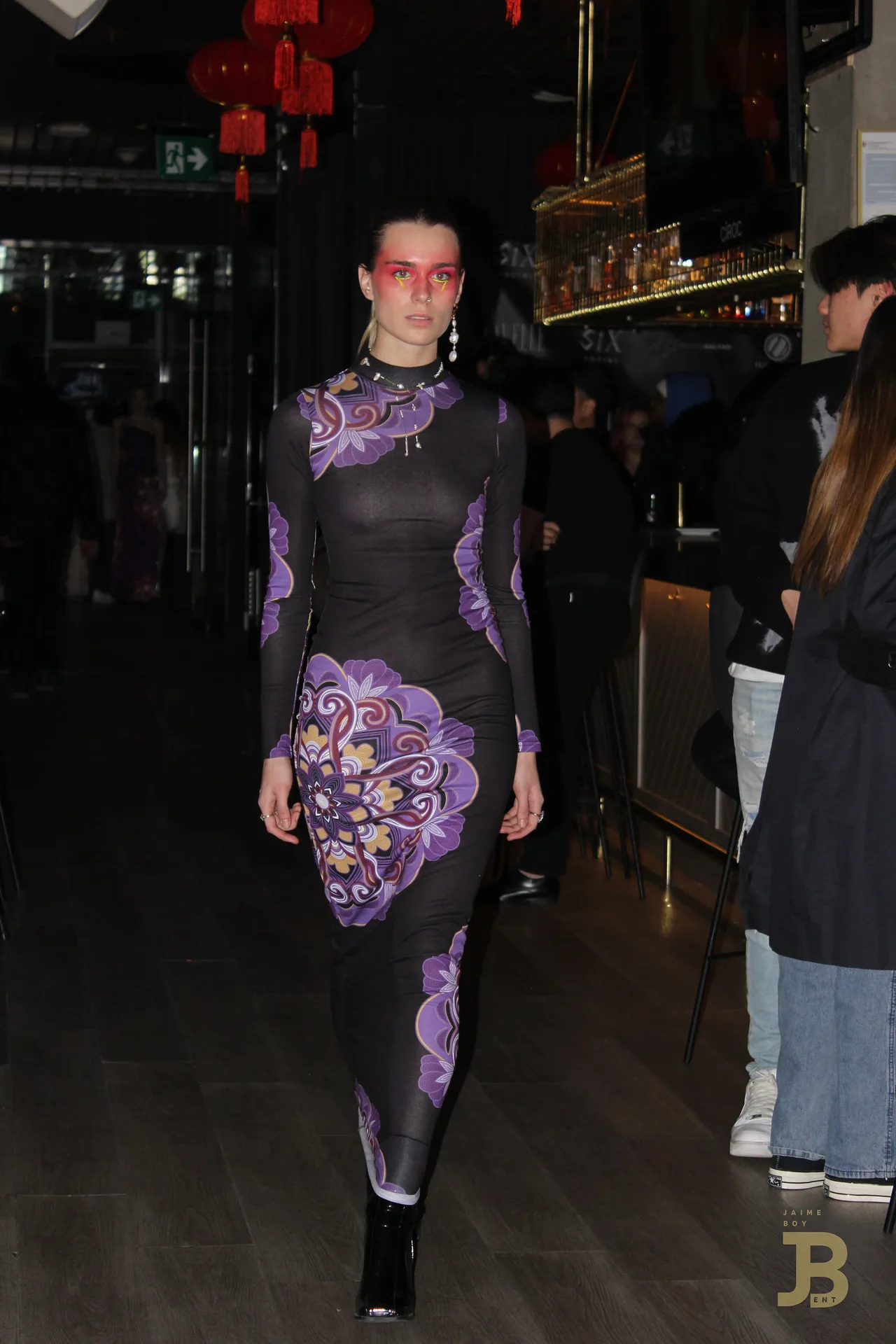 A model in a purple floral bodycon dress with red eye make-up on the runway.