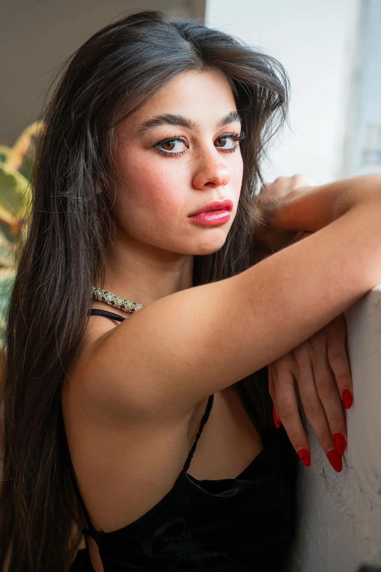 Close portrait of a model with long dark hair resting her arms on a white ledge.