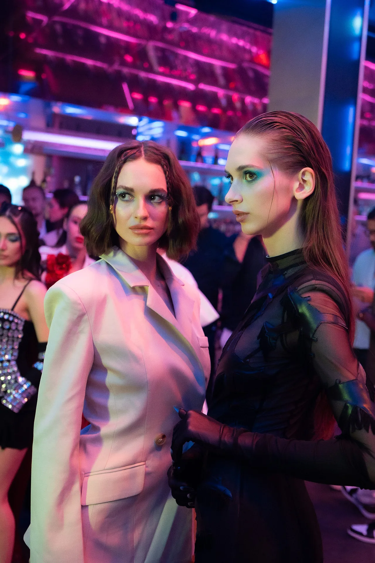 Two models with graphic green eye make-up, one in a white blazer, one in black.