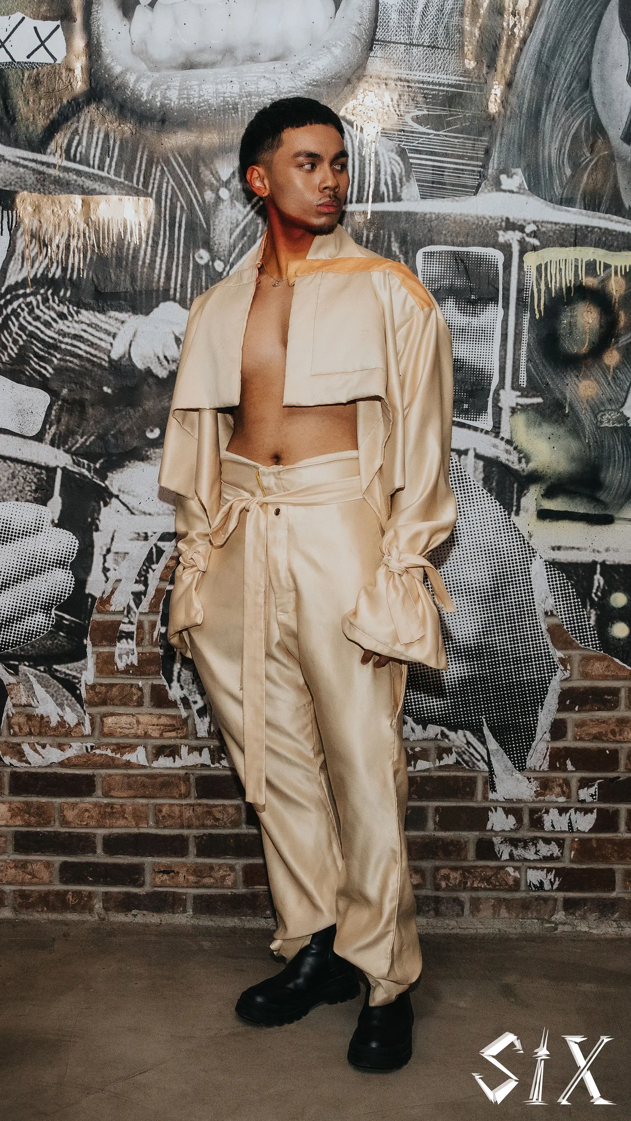 A model in a cream cropped jacket and wide trousers in front of a mural.