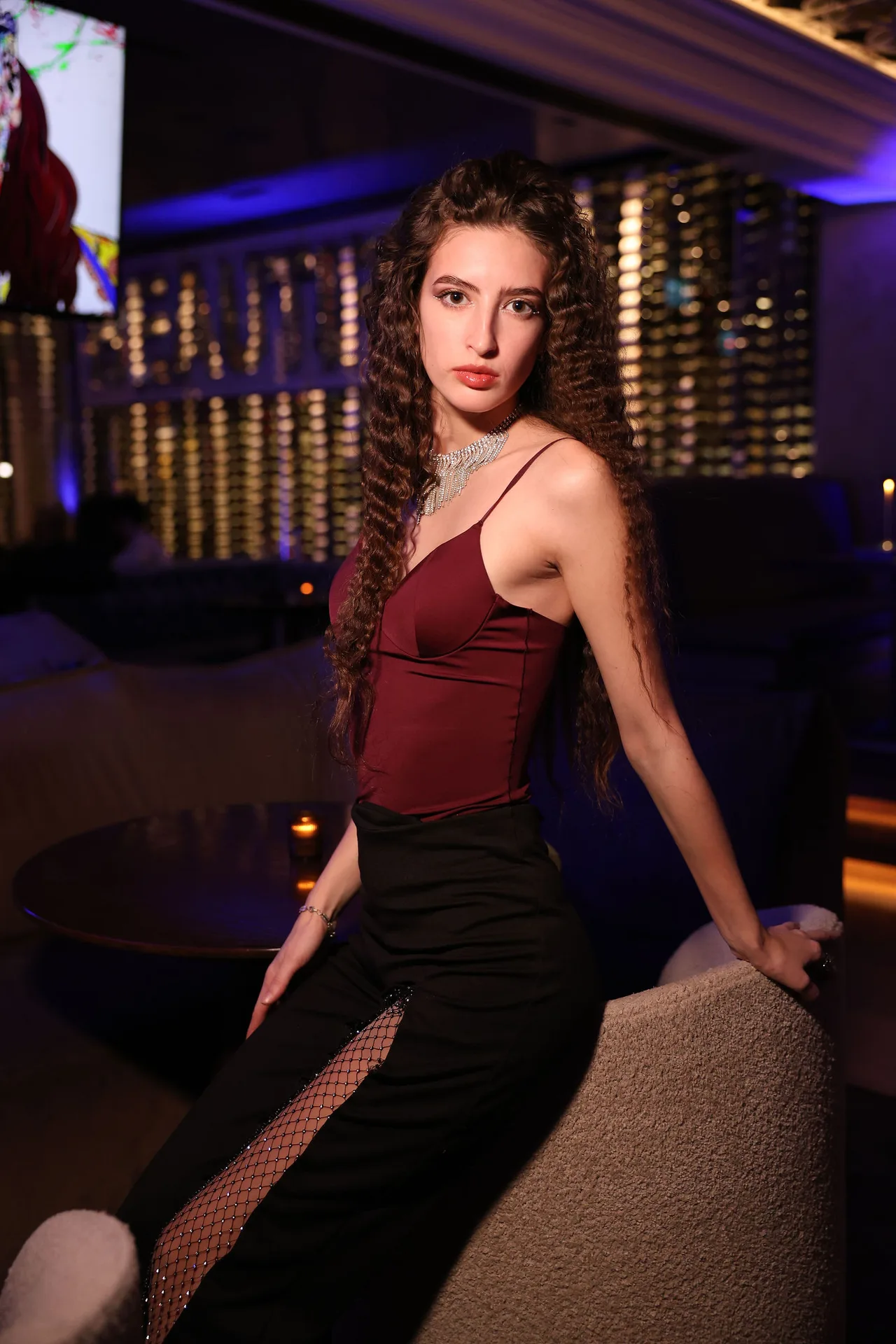 A guest in a burgundy top and lace-panelled skirt seated in a boucle chair.