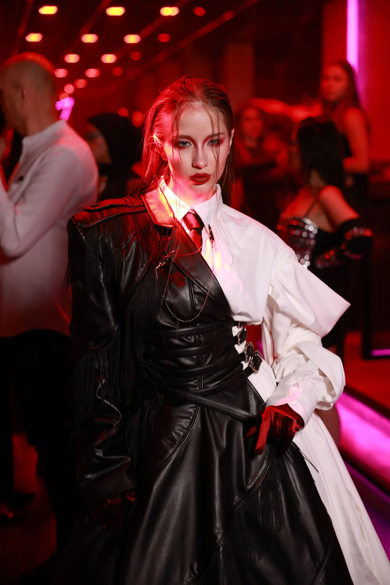 A model in a split black leather and white coat with a red tie, lit in red.