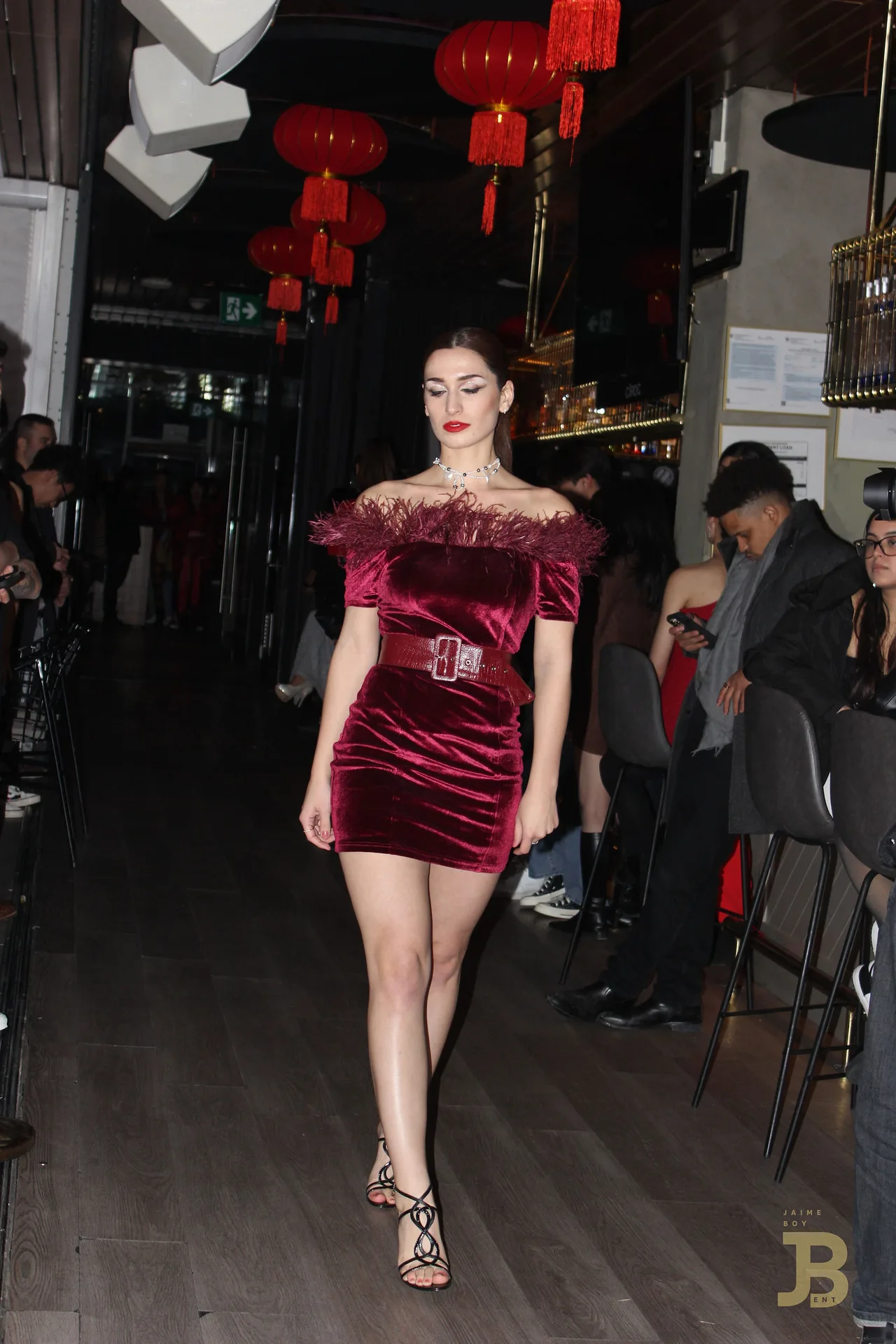 A model in a burgundy velvet off-shoulder mini dress with a belt.