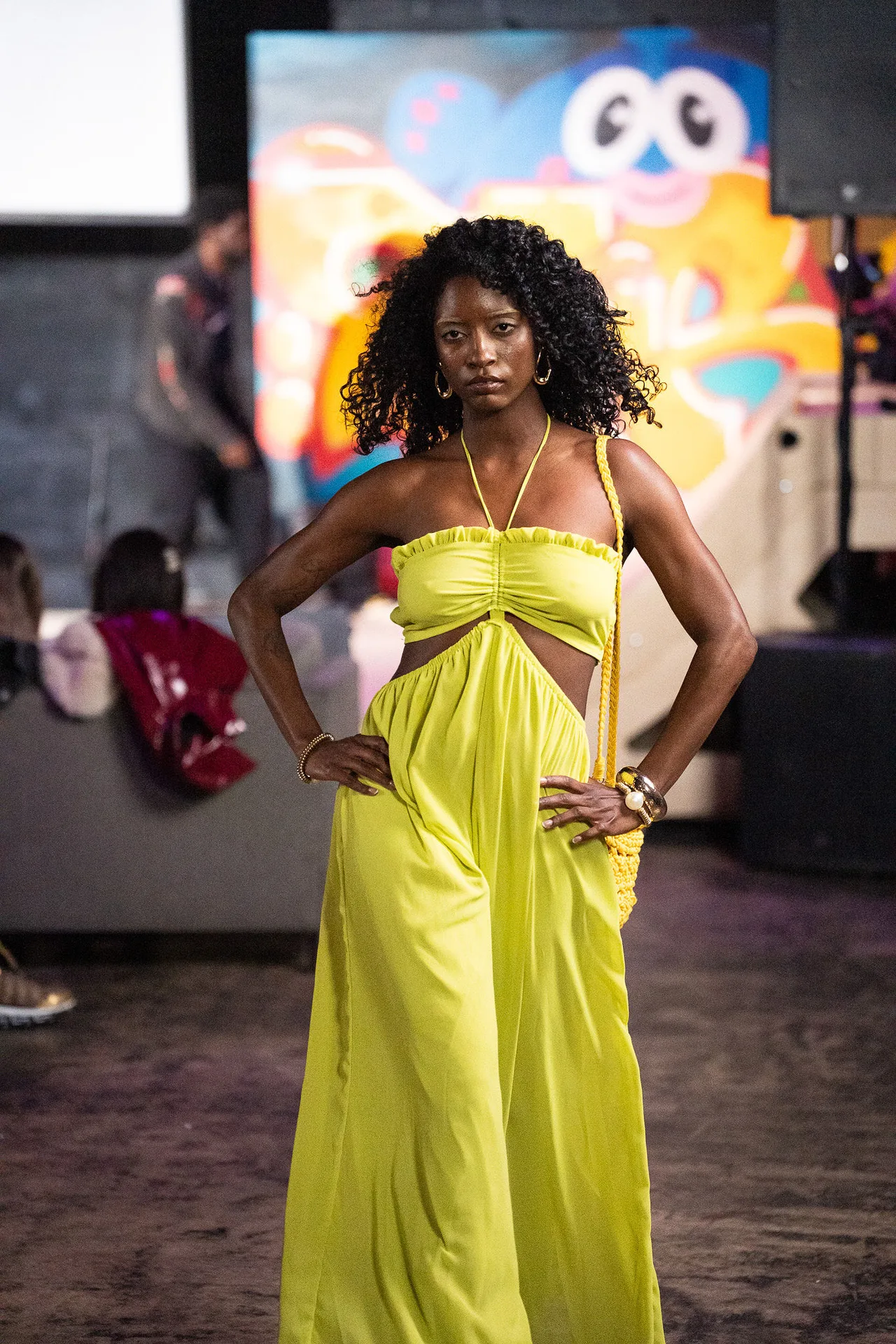 A model in a chartreuse halter jumpsuit with cut-outs, hands on hips.