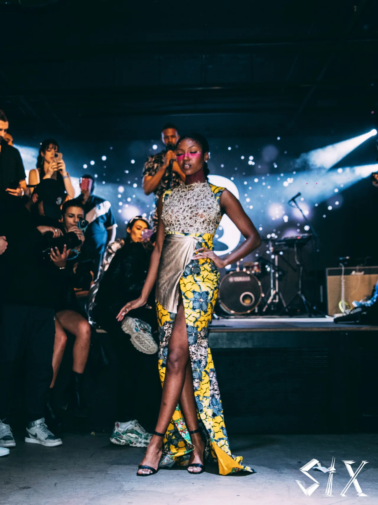 A model in a print gown with a high slit walking under stage lights.
