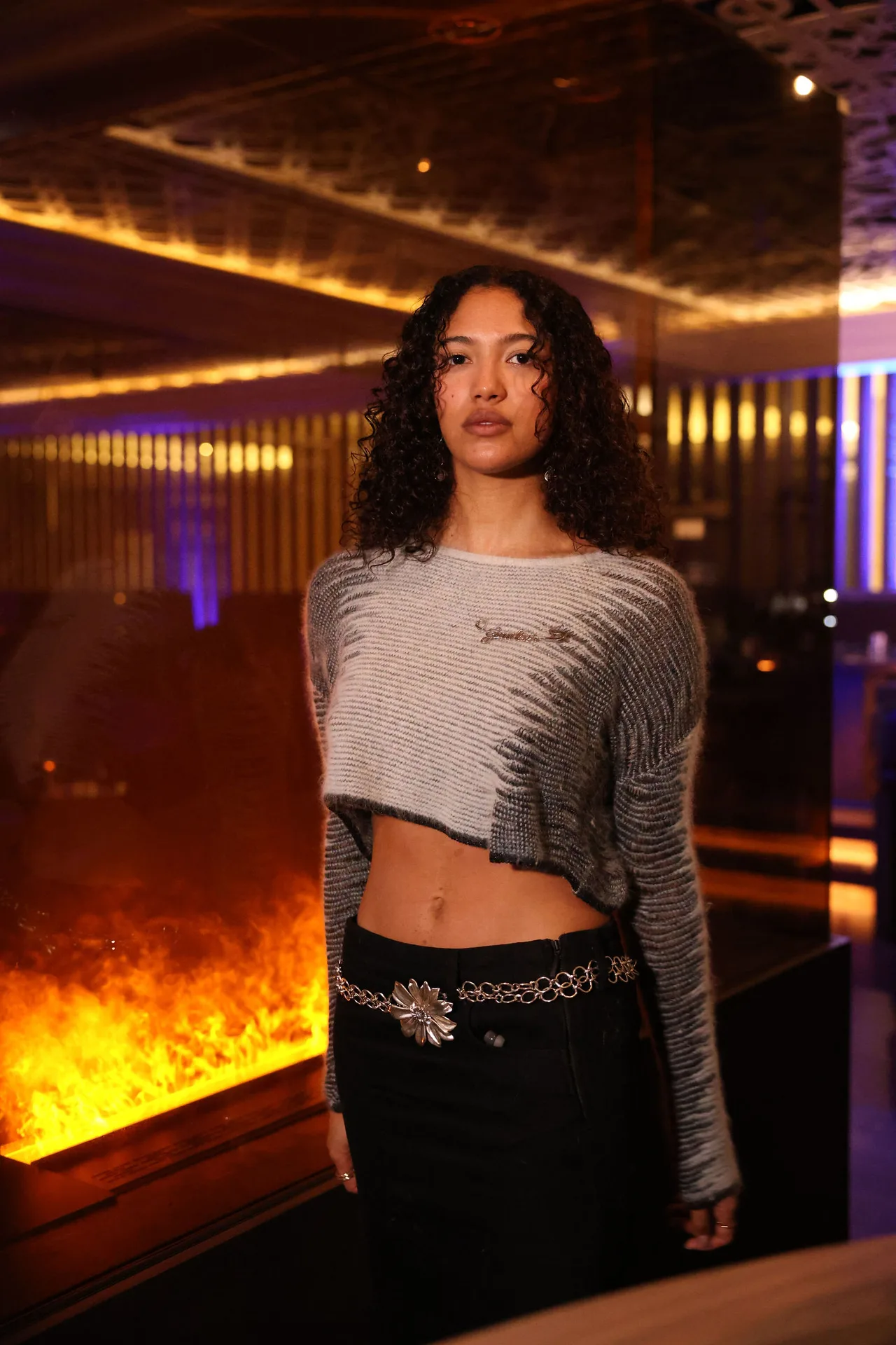 A guest in a striped cropped sweater and black skirt in front of a fire feature.