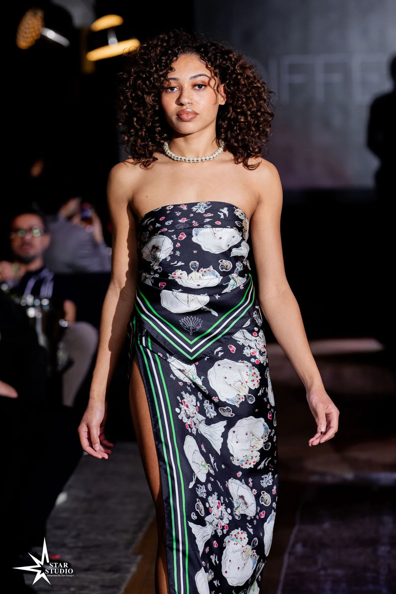 A model in a strapless black-and-white floral print dress with a high slit and pearls.