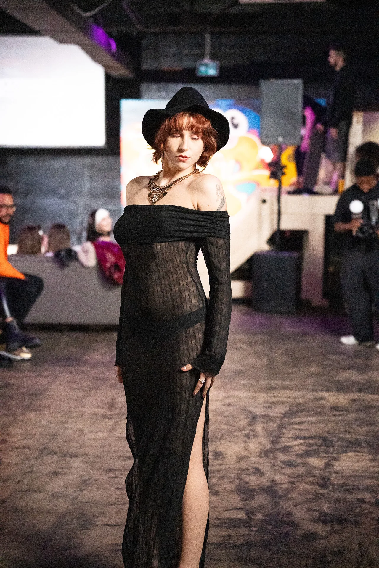A model in a black lace off-shoulder gown and wide-brim hat.