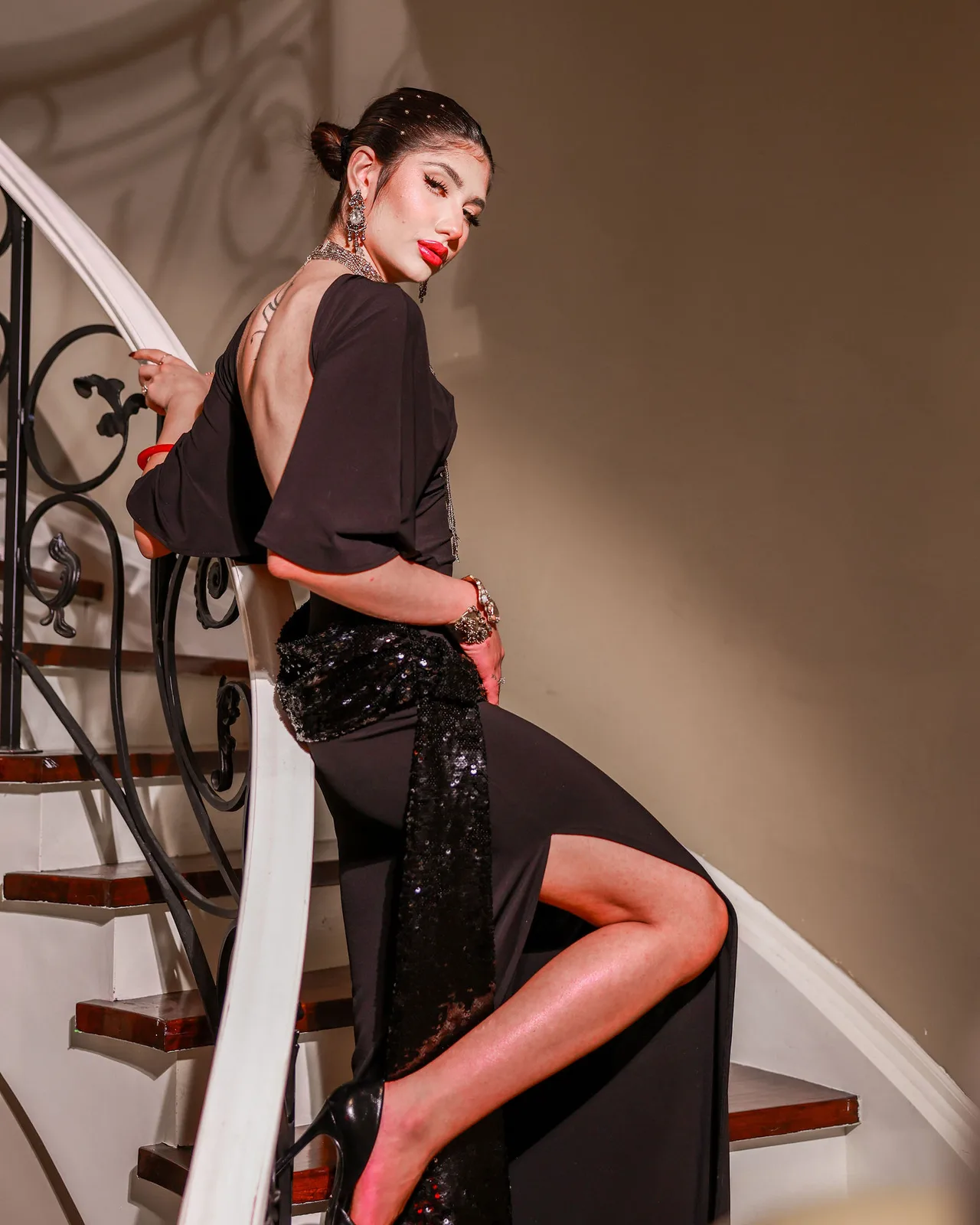 A model in a backless black dress posing on a curved staircase.