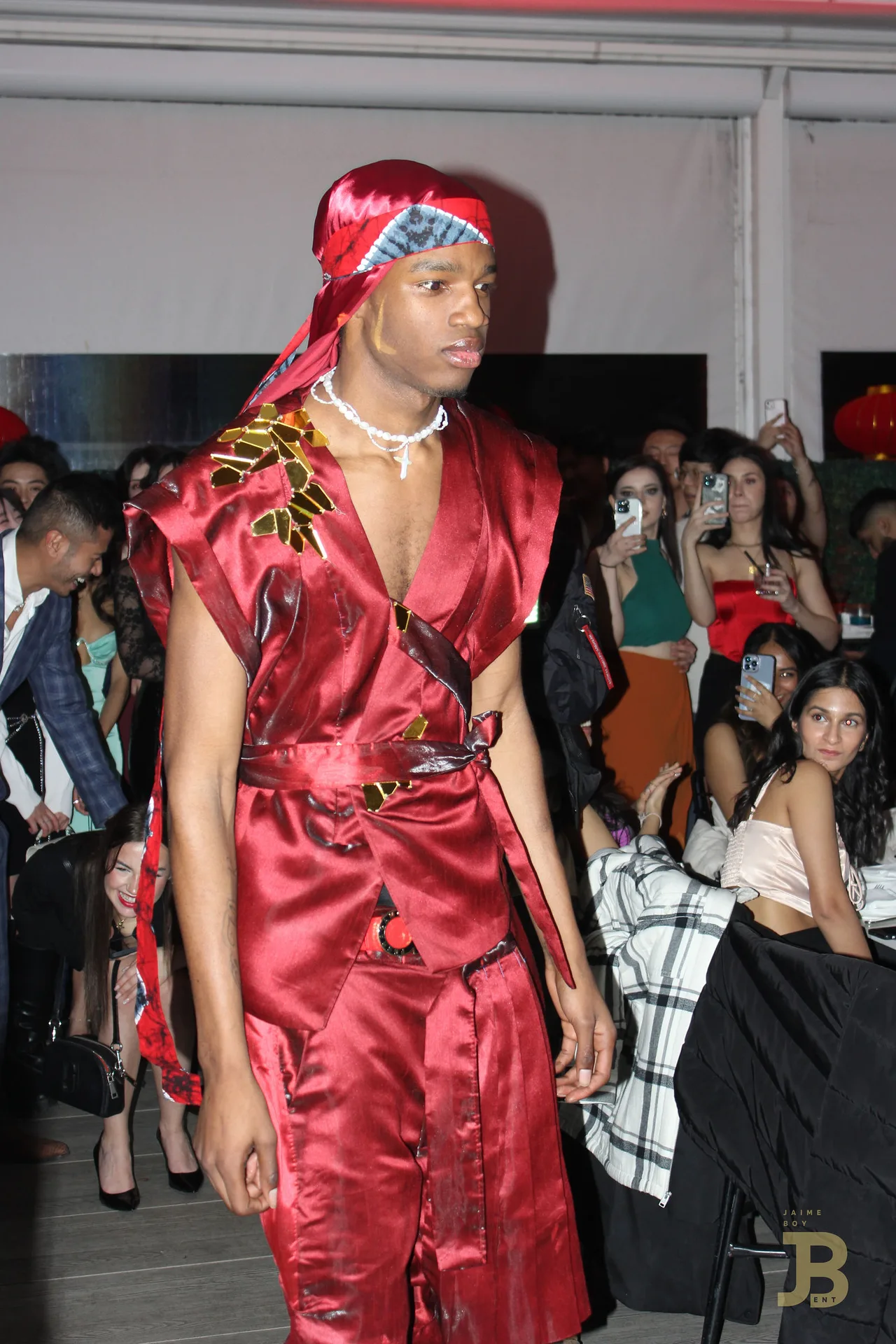 A model in a red satin robe and headscarf with a pearl necklace.