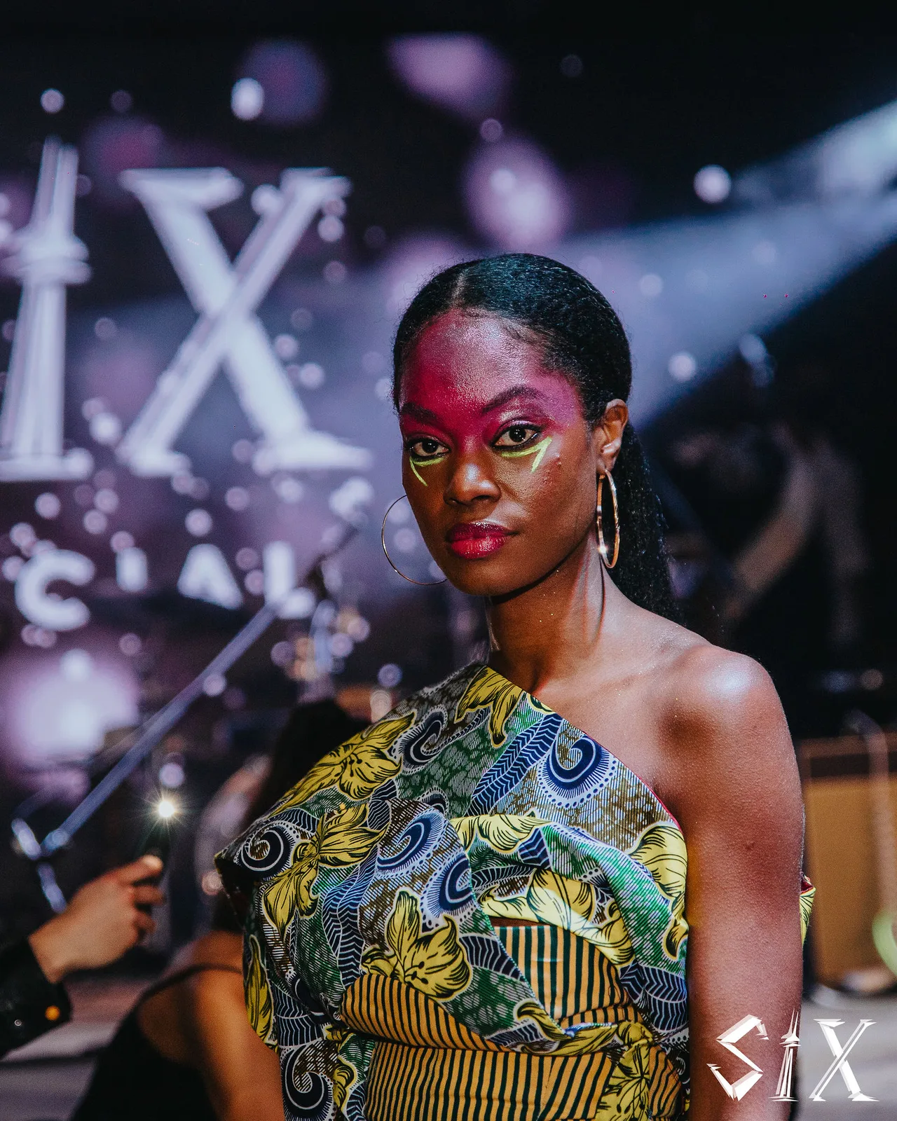 Portrait of a model with red and gold face paint in a printed dress.