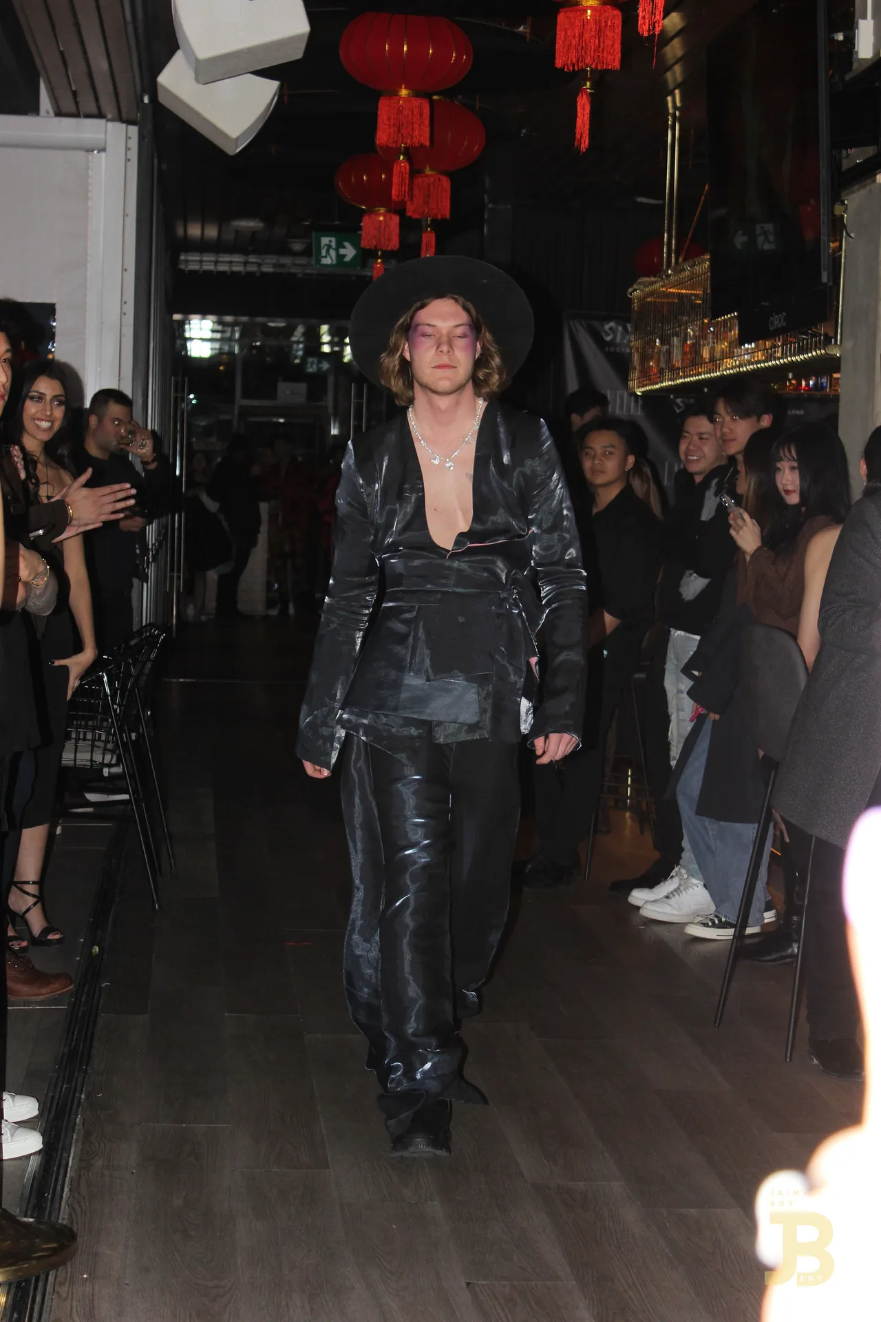 A model in black satin with a wide-brim hat walking the runway.