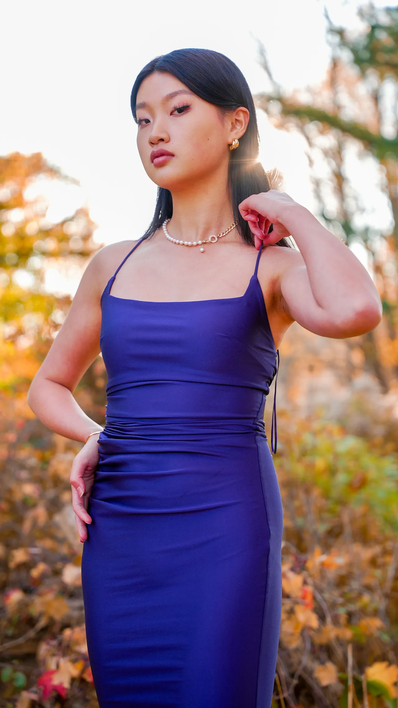 Portrait of a model in a purple satin dress against autumn leaves.