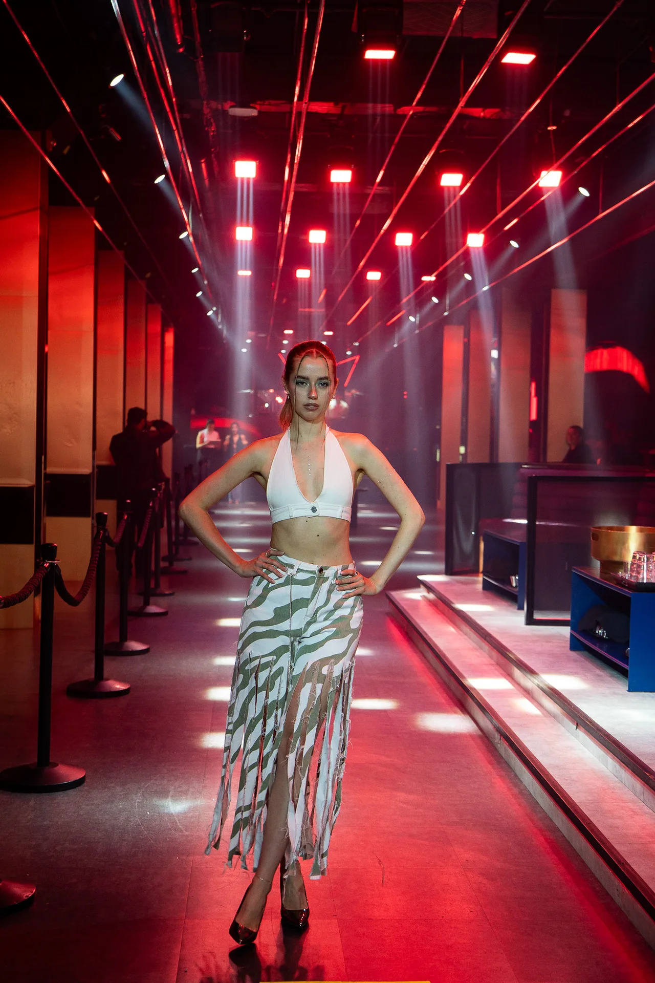 A model in a white halter top and zebra-print skirt walking a runway of red lights.