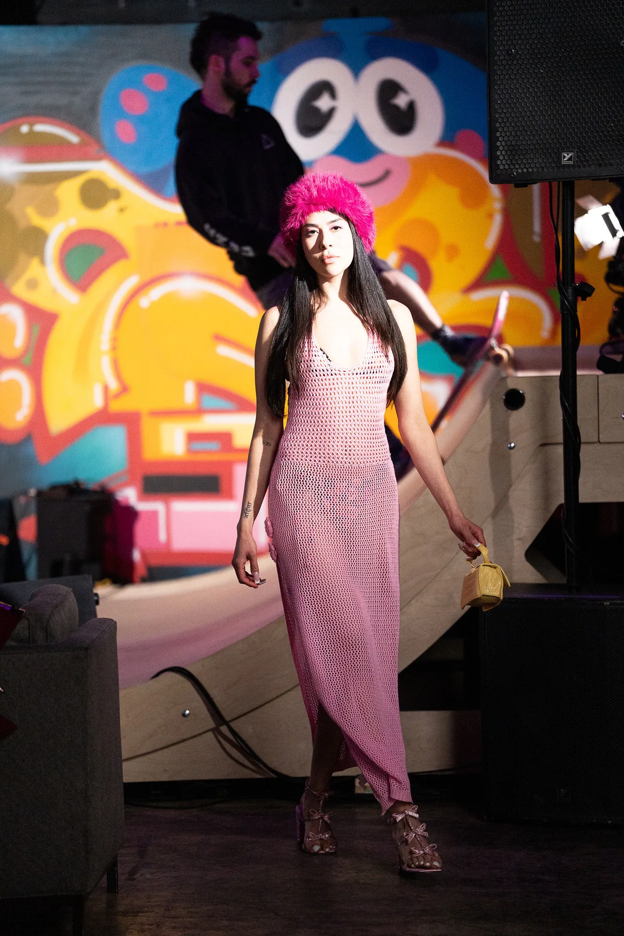 A model in a pink crochet dress and fluffy pink hat against a graffiti mural.