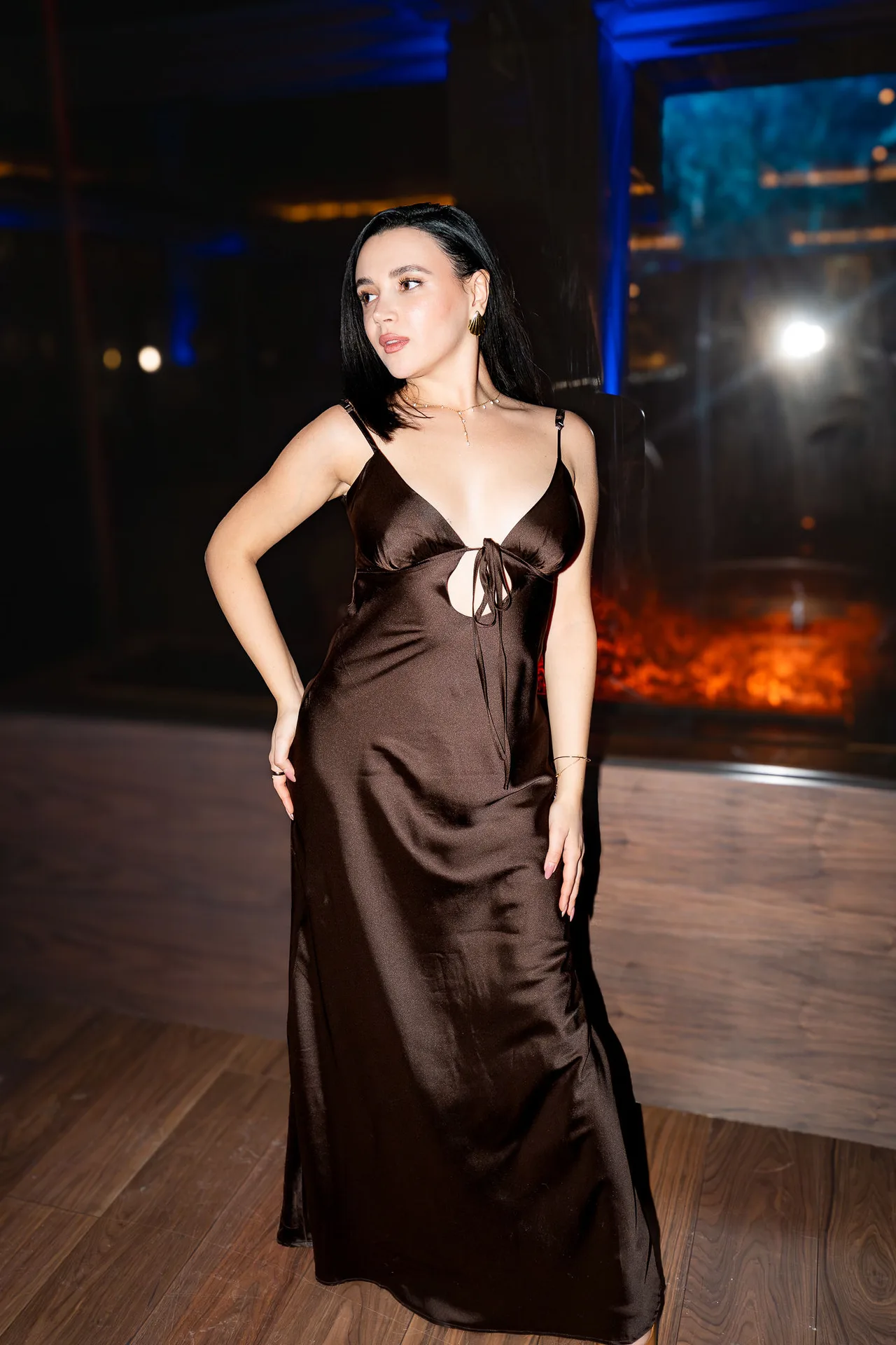 A guest in a chocolate satin slip dress beside a glowing fire wall at Blue Bovine.