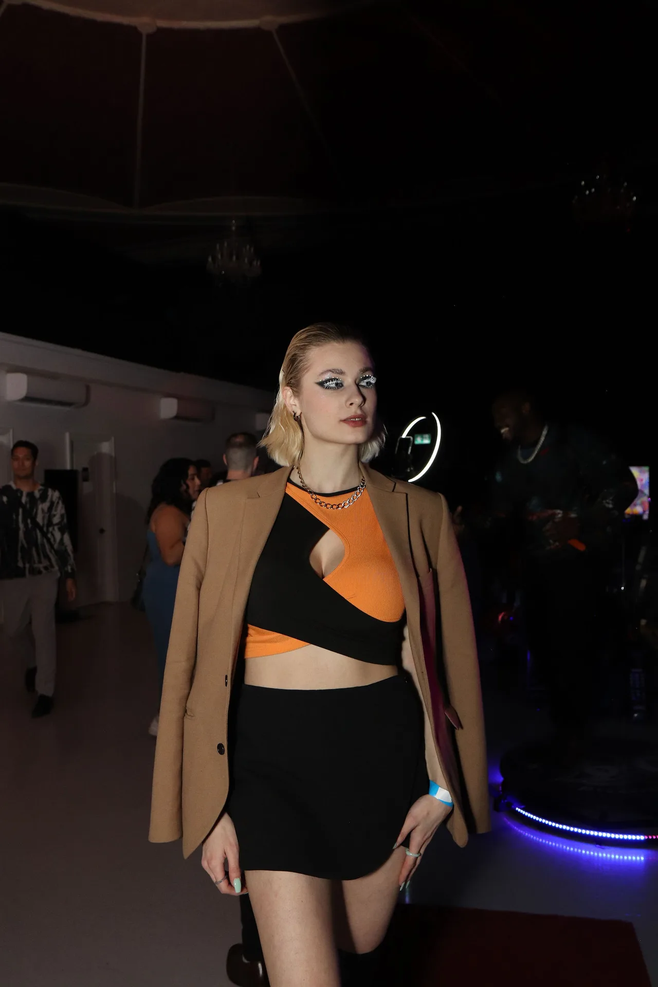 A model in a camel blazer over an orange and black top.