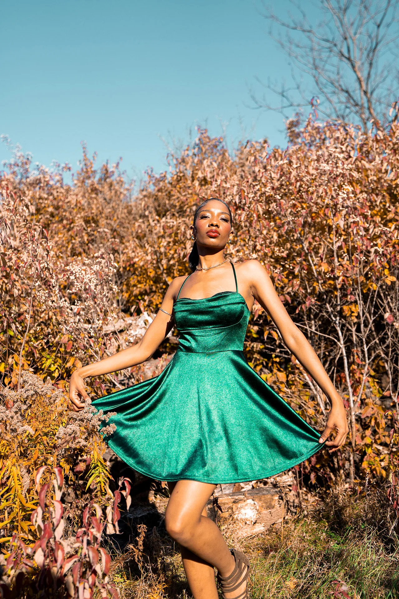 A model in an emerald satin dress caught mid-spin among autumn shrubs.