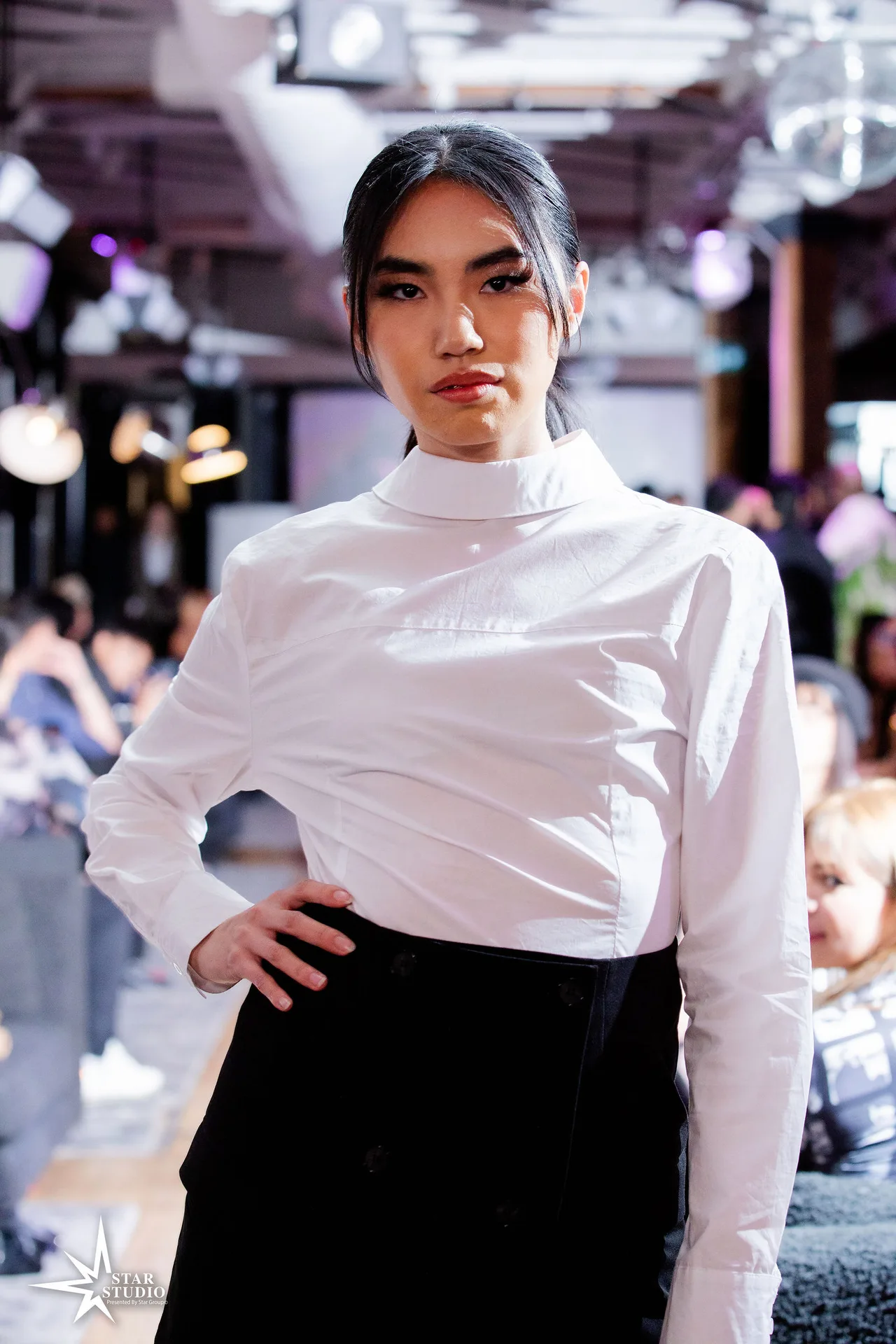 A model in a white high-neck shirt and black skirt.