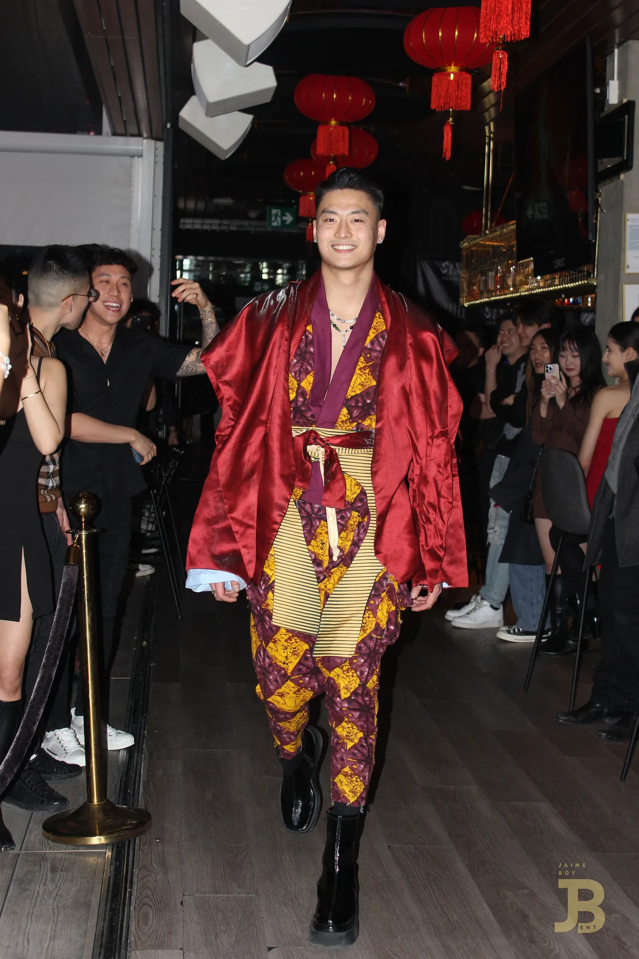 A model in a red satin robe over a gold patterned outfit on the runway.