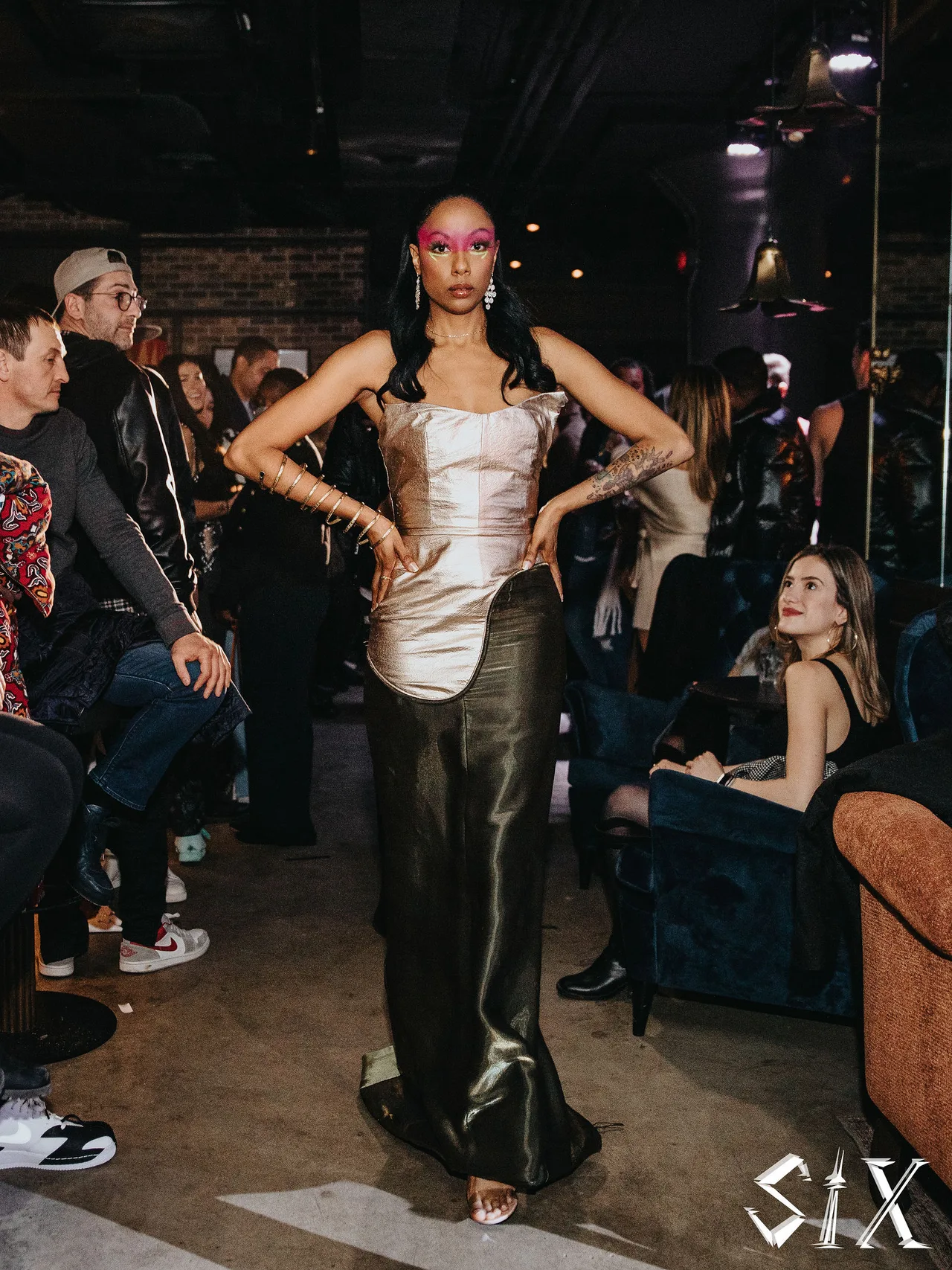 A model in a silver corset top and olive satin skirt walking among guests.