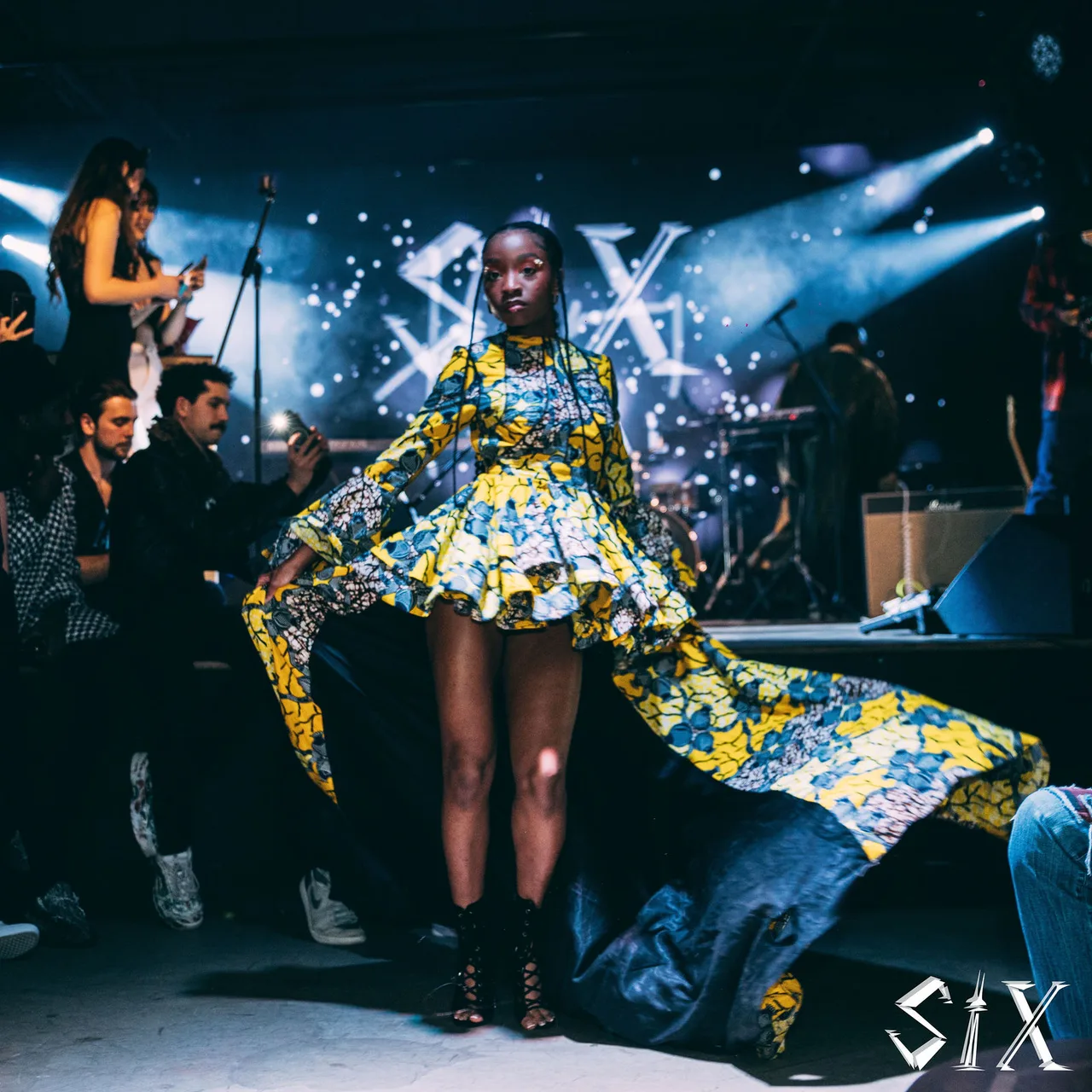 A model in a yellow and blue print dress with a flowing train mid-stride.