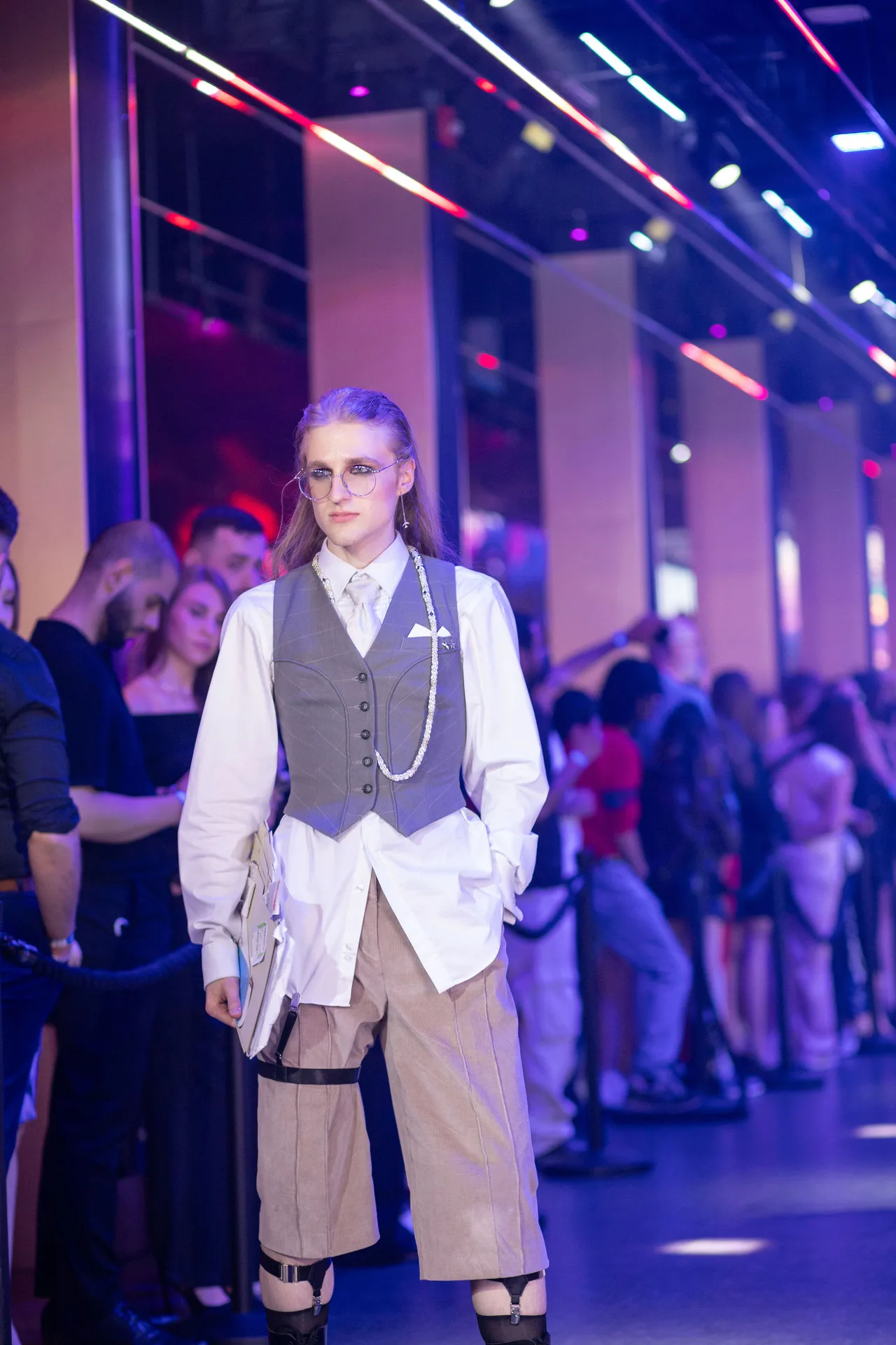 A model in a grey waistcoat, white shirt and cream trousers on the runway.