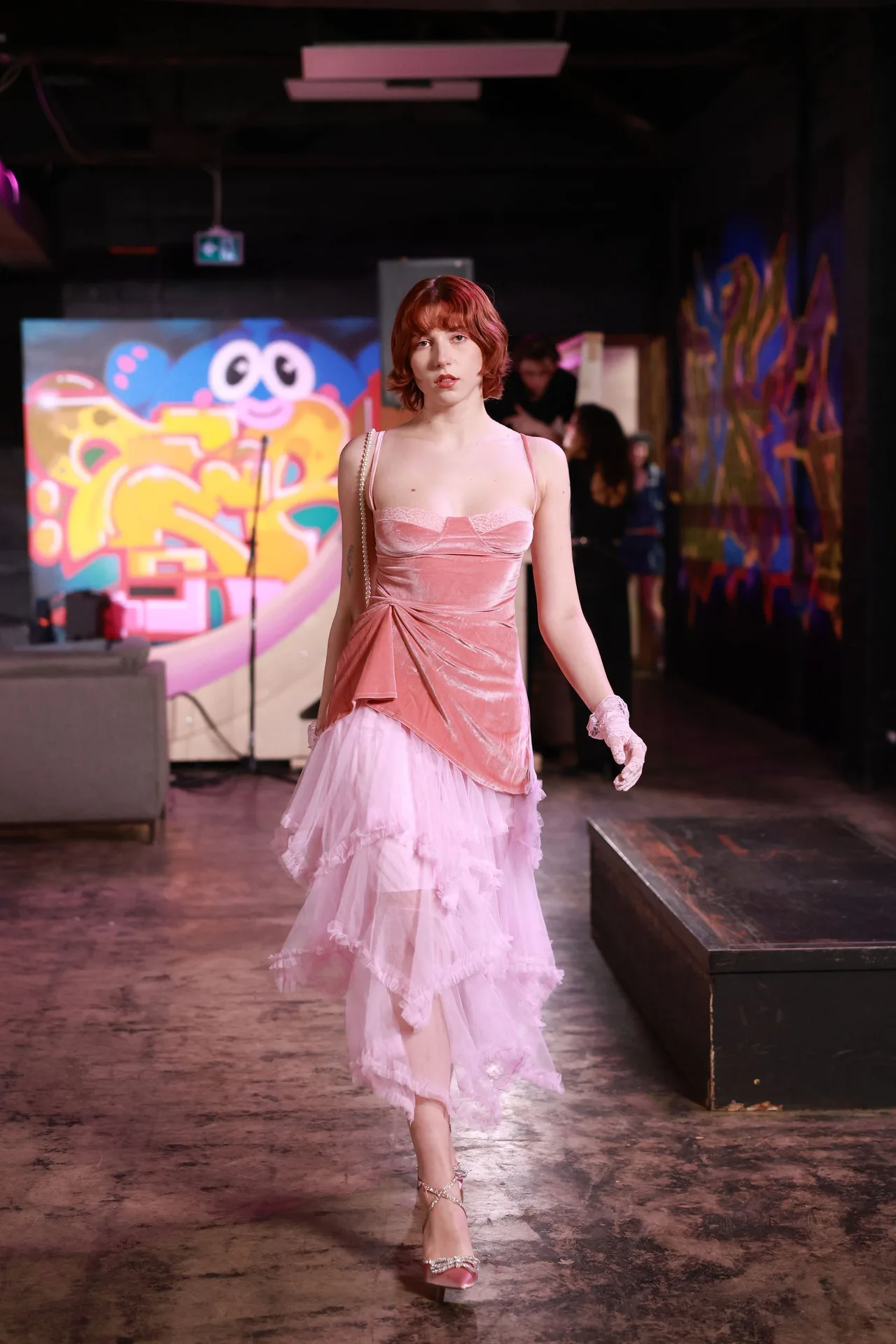 A model in a pink velvet top and layered tulle skirt walking the floor.