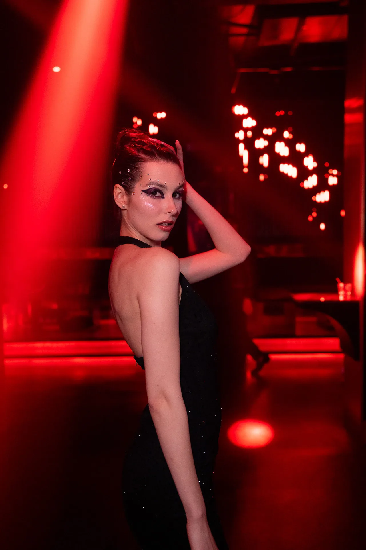 A model in a backless black dress looking over her shoulder in red light.