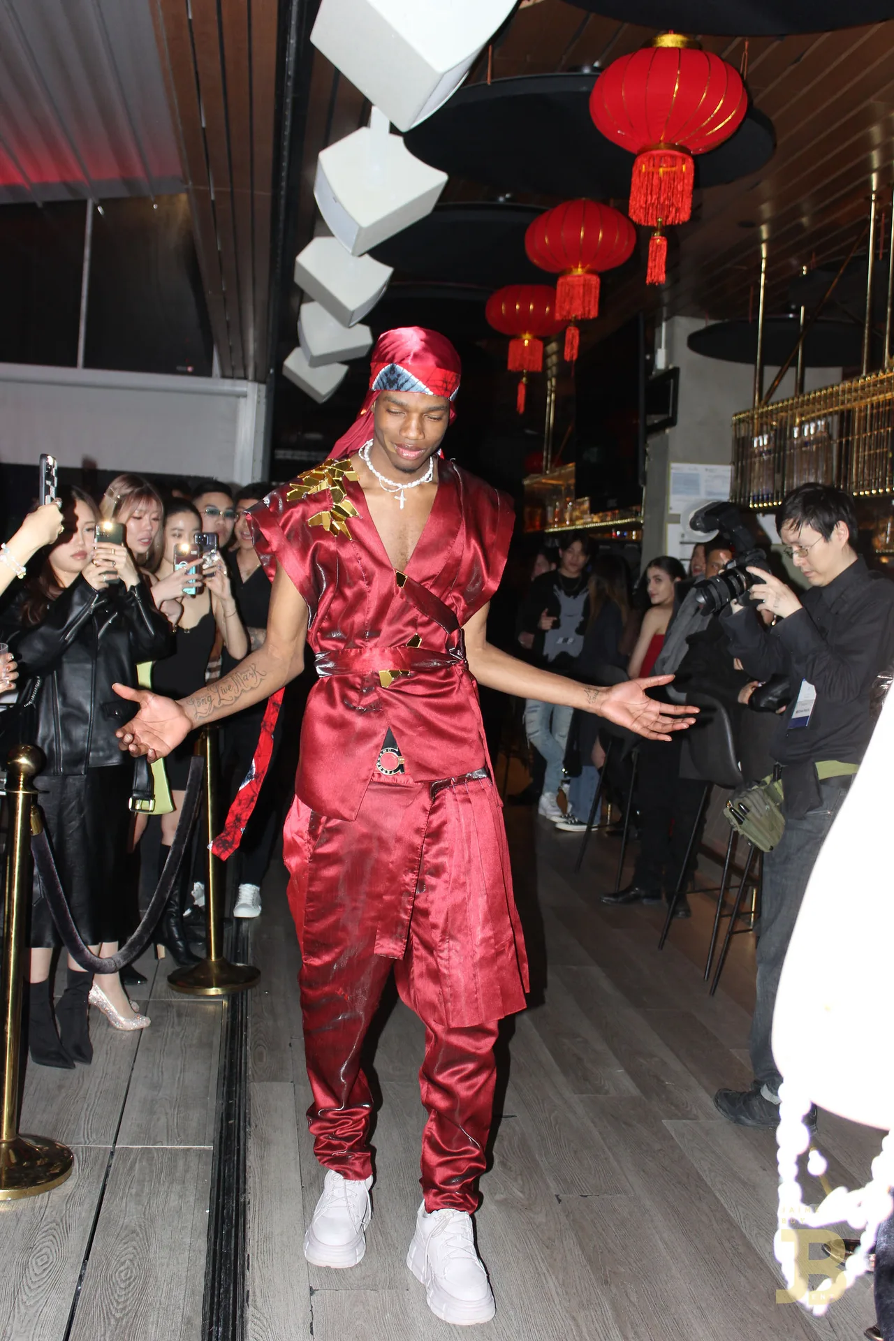A model in a red satin suit and headscarf striking a pose on the runway.