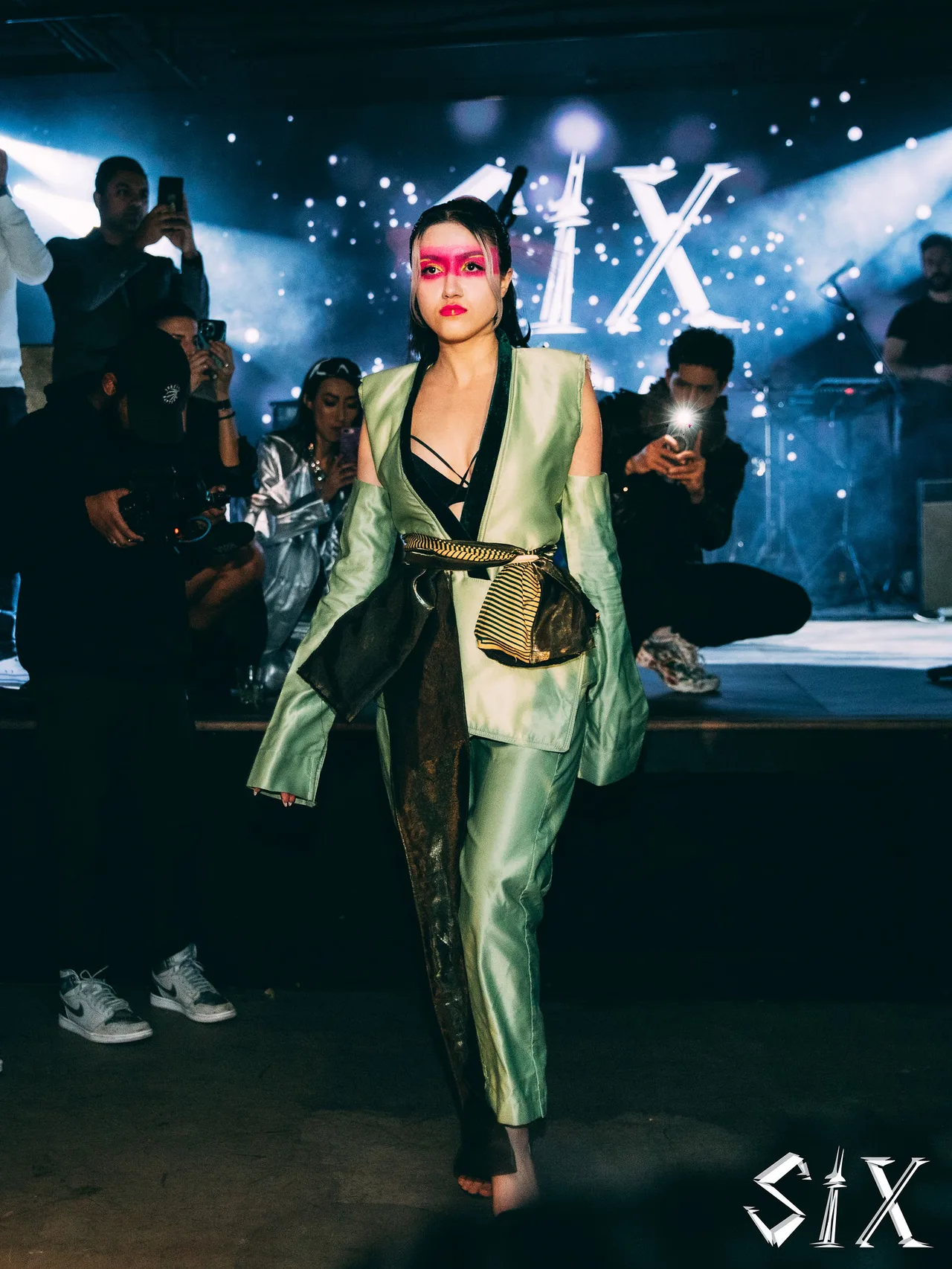A model in a mint satin suit with pink eye make-up on the runway.