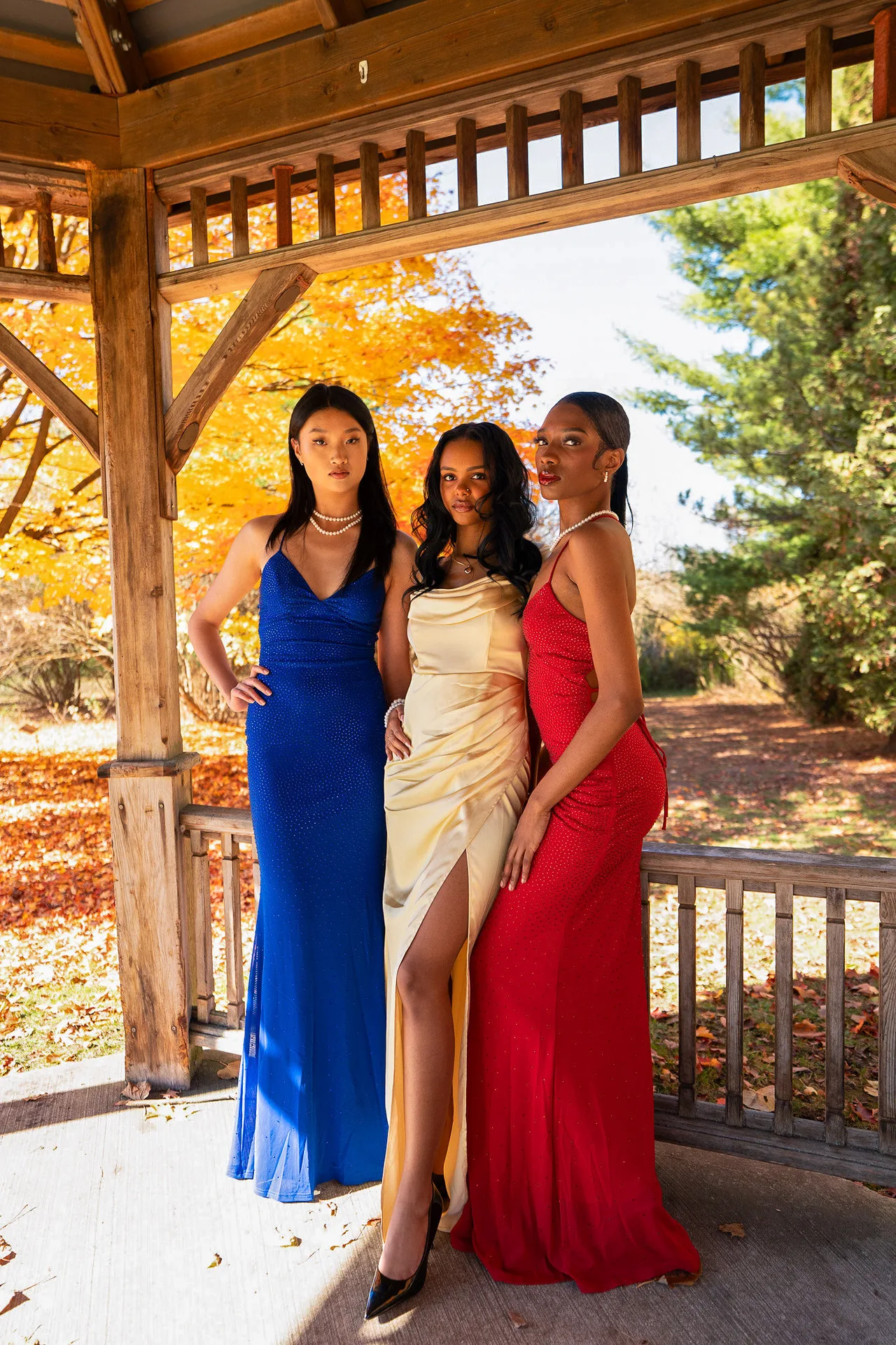Three models in blue, champagne and red gowns in a wooden gazebo.